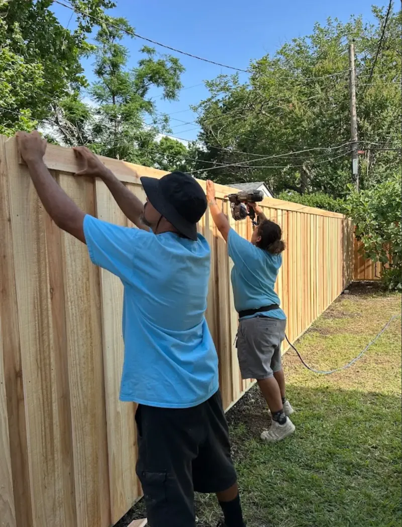 Crew setting cedar pickets along a finished fence line.